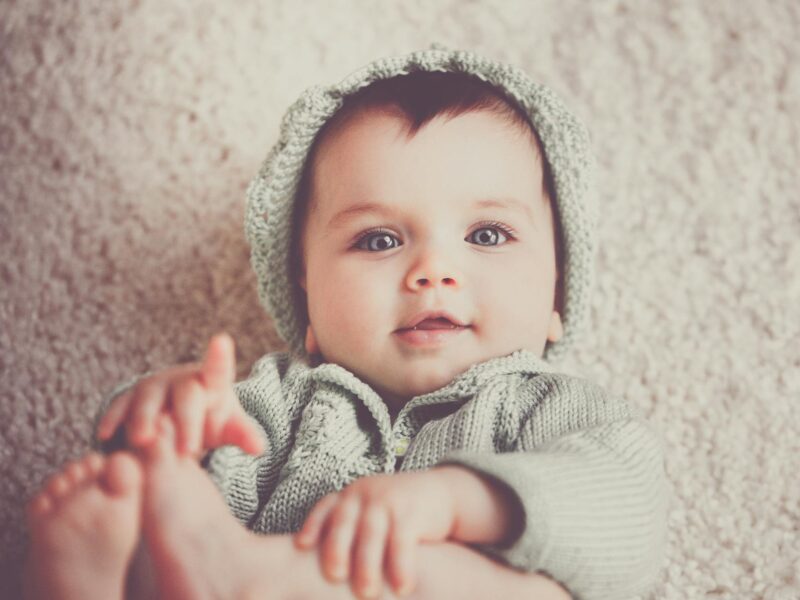 baby on gray knit hooded clothes lying on carpet