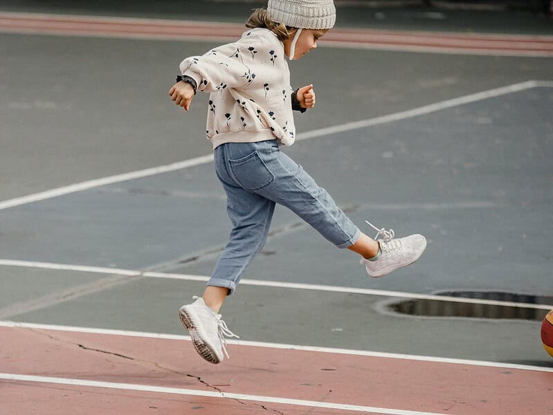 little girl jumping while playing with ball on sports ground